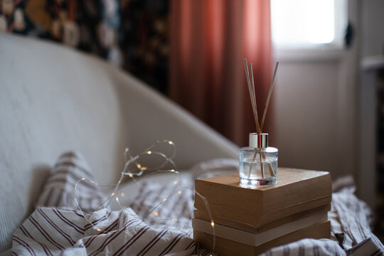 Aroma liquid glass bottle diffuser with wooden sticks on stack of old paper books in living room at dusk light. Aromatherapy.