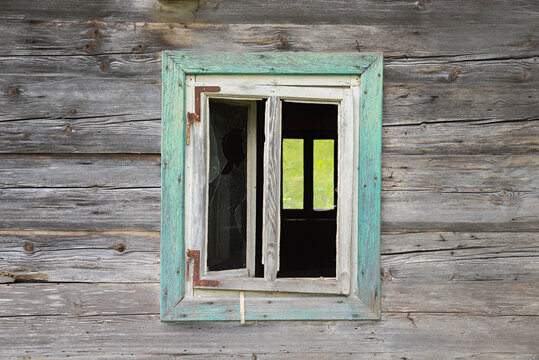 Weathered wooden facade with a window, broken glass pane. Abandoned house.