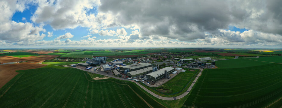 Aerial view of grain storage silos and a water treatment plant surrounded by vast agricultural fields under a cloudy sky in Hemswell Cliff, England, United Kingdom.