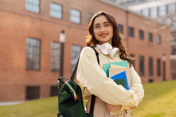 Fototapeta premium Happy European lady student with backpack and notepads exercise books posing outdoor at university campus, smiling at camera, copy space. Students lifestyle concept