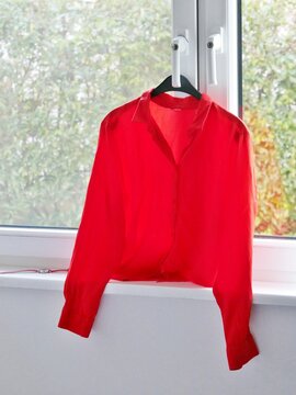 Rote Bluse h&auml;ngt auf B&uuml;gel am Fenster zum Ausl&uuml;ften
