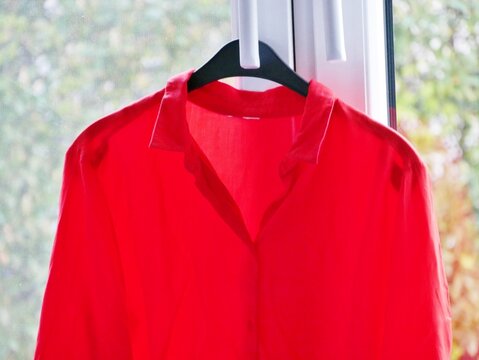 Rote Bluse h&auml;ngt auf B&uuml;gel am Fenster zum Ausl&uuml;ften