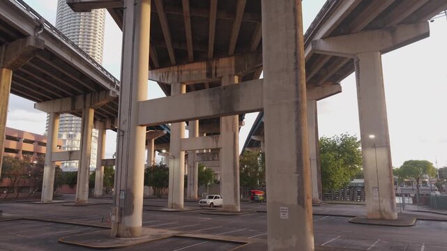 Underneath rows of concrete columns supporting three elevated expressway lanes and parking lot in the bottom