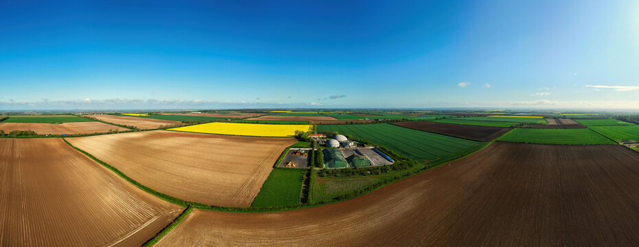 Aerial view of FBG Grange Farm Energy Spridlington surrounded by vibrant yellow rapeseed fields, green pastures, and tilled soil under a clear blue sky Market Rasen, England, United Kingdom.
