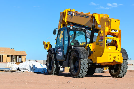 Telescopic handler parked at a residential construction site in a housing development, representing material handling, equipment staging, and suburban building operations