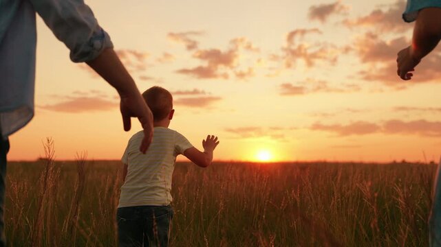 Father, mother, child run through tall grass outdoors. Dad mom chase little son while playing outdoors. Happy family. Mom dad, kid son picnic outdoors on weekend. Parents, kid boy, play together