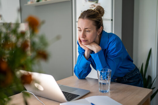 Thoughtful mature woman engaged in learning process online on laptop at home, female watching professional speakers live streams and podcasts, lady changing career direction, getting new knowledge.