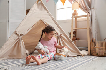 Little girl playing with toys near toy wigwam in playroom, space for text © New Africa