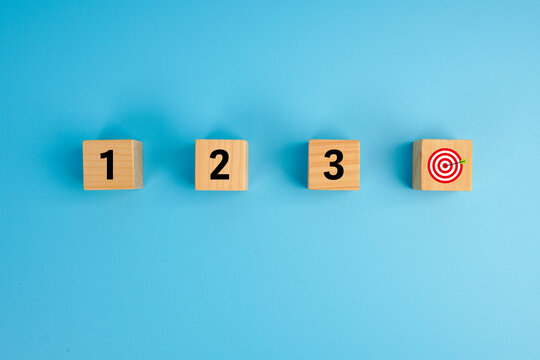 Step-by-step progress and goal achievement concept. Wooden cubes labeled 1, 2, 3 leading to a target icon, symbolizing planning, sequence, strategy, execution, and successful outcomes.