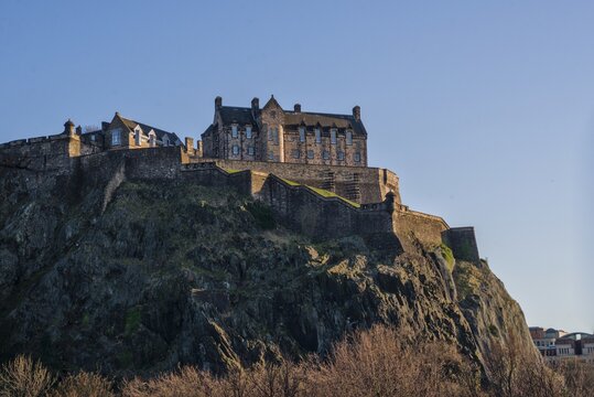 Edinburgh Castle perched dramatically on volcanic rock under a warm golden sky at dusk or sunset, Scotland.