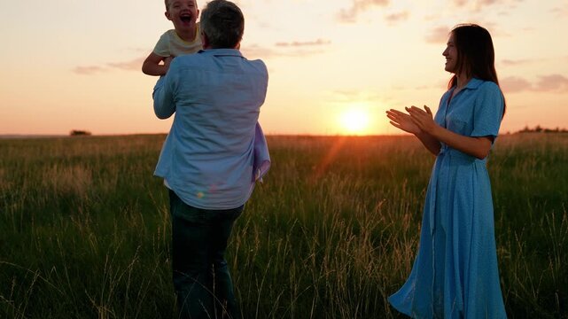 Parents, mom dad, play, spin with their little son, holding hands, on lawn sun. Mom dad, kid relaxing in nature park. Family picnic in nature. Childhood dream concept. Father, mother, raising child.