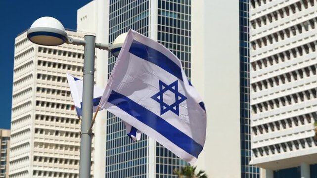 Israeli flag waving in the wind in front of the iconic Shalom Meir Tower in Tel Aviv, Israel. A symbol of national pride against the backdrop of a major city landmark during a bright sunny day now

