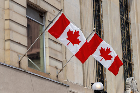 Ottawa, Canada - July 1, 2025: Two Canadian flags hanging from historic stone building. National flags of Canada displayed on urban architecture