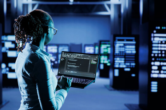 Experienced specialist running code and programming on laptop, troubleshooting and upgrading high tech facility designed to accommodate multiple clusters of fully operational server cabinets