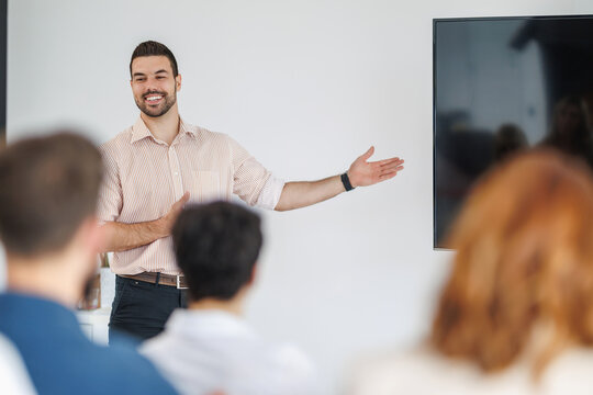 Man gives a presentation in a modern office while an audience listens and engages during a corporate training session