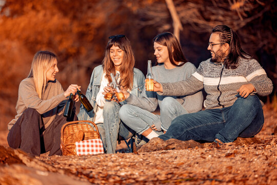 Friends enjoy a picnic by the riverbank during warm autumn afternoon while sharing drinks and food