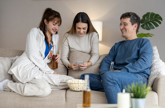 Friends enjoy snacks and watching videos together on a couch in a cozy living room in the evening