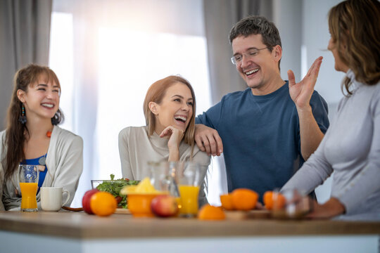 Friends gather for a casual breakfast in a bright kitchen with fruits and drinks around them