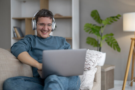 Man using laptop and wearing headphones while sitting on a couch in a bright living room during the day