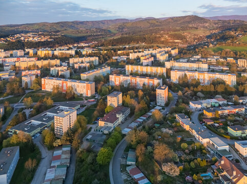 Aerial view of the Spojova residential area with apartment buildings surrounded by lush green trees and rolling hills under a soft sunset light in Banska Bystrica, Banskobystricky kraj, Slovakia.