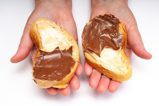 Two hands holding slices of bread spread with creamy chocolate topping, symbolizing sweet indulgence and snack choice. 