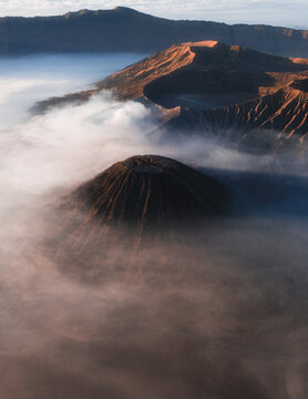 Aerial view of Bromo Tengger Semeru National Park with volcanic craters emerging from thick morning mist under golden sunrise light Bromo, East Java, Indonesia.