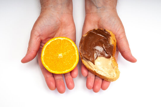 Orange half in one hand and bread slice with chocolate cream spread in the other