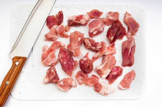 Pieces of raw meat and a kitchen knife on a modern white cutting board with dotted textures