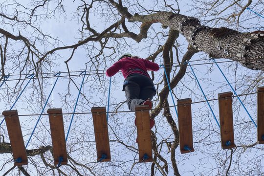 Person in helmet and harness crossing suspended obstacle on rope course between trees