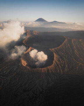 Aerial view of the smoking crater of Mount Bromo within the vast Tengger caldera under a soft morning light with Mount Semeru in the distance Bromo, East Java, Indonesia.