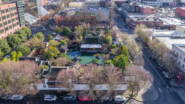 Aerial view of Lan Su Chinese Garden with traditional pavilions, a central pond, and lush greenery surrounded by urban city streets Portland, Oregon, United States.