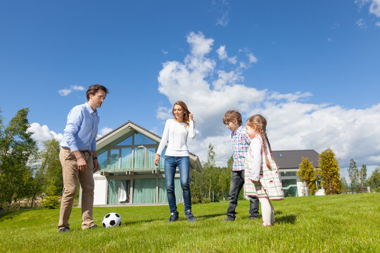 Family playing soccer on lawn in front of modern house