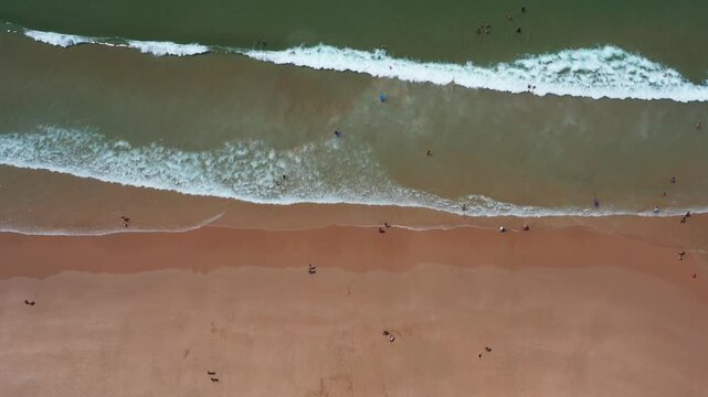 People enjoying various activities on the beach near Caparica in Portugal. The aerial view captures the waves, sand, and beachgoers at different times.