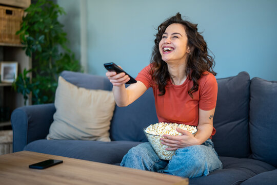 Happy woman laughing watching television holding popcorn and remote