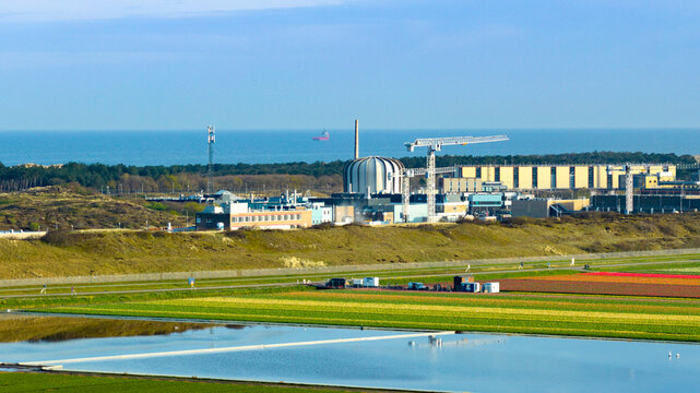 Aerial view of the High Flux Reactor nuclear facility with construction cranes, coastal dunes, and colorful tulip fields Petten, North Holland, Netherlands.