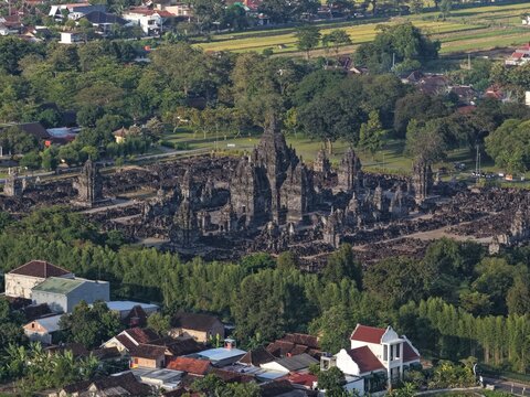 Aerial view of the ancient Prambanan Temple complex with its towering stone spires surrounded by lush greenery and residential houses in Kecamatan Prambanan, Daerah Istimewa Yogya, Indonesia.