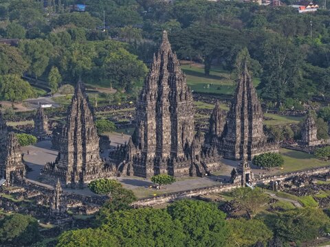 Aerial view of the intricate stone spires of Prambanan Temple surrounded by lush green trees and parkland in Kecamatan Prambanan, Daerah Istimewa Yogya, Indonesia.