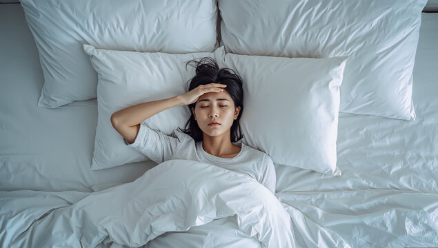 白いベッドで眠れない日本人女性を表現した不眠イメージ写真