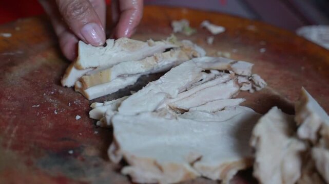Cooked chicken being chopped on a wooden cutting board, close-up Asian street food preparation with cleaver and tender meat.