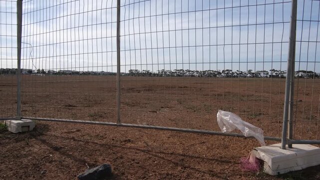 A vast expanse of cleared and dry bare soil on a large undeveloped land parcel viewed through a temporary steel mesh security fence in Tarneit, Melbourne, Australia.