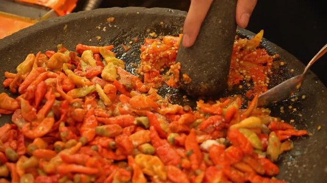 Fresh red chilies crushed in stone mortar, spicy sambal preparation with vibrant colors and authentic Asian street food vibe.