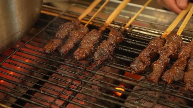 Grilled beef satay skewers over charcoal fire, smoky street food BBQ with golden brown meat, close-up cinematic cooking shot.