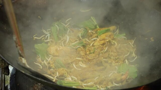 Stir-fried flat rice noodles with bean sprouts and greens in a hot wok, smoky Asian street food close-up.