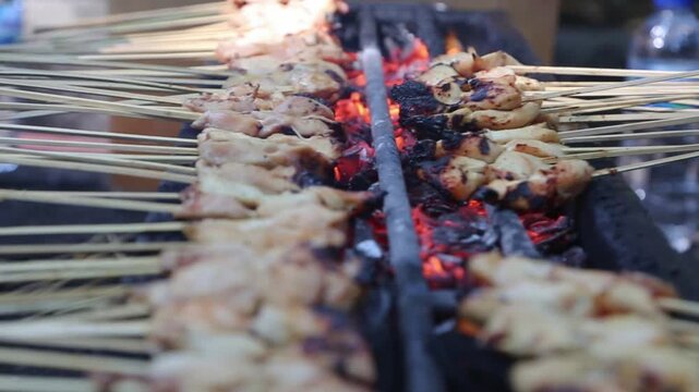 Chicken satay skewers grilling over glowing charcoal, smoky Asian street food BBQ with juicy meat and close-up cooking.