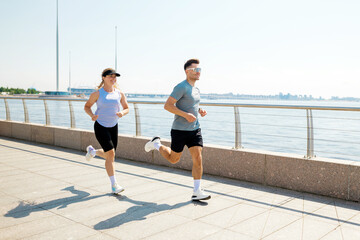 Obraz premium Joyful couple runs along the waterfront path, embracing sunlight on a bright day in a vibrant outdoor setting