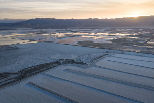 Aerial view of Searles Lake featuring salt evaporation ponds and geometric patterns against distant mountains under a golden sunset sky San Bernardino County, California, United States.