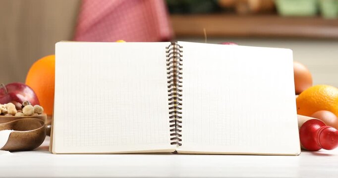 Open recipe book, kitchen utensils and fresh products on white table indoors, closeup. Camera zooming out