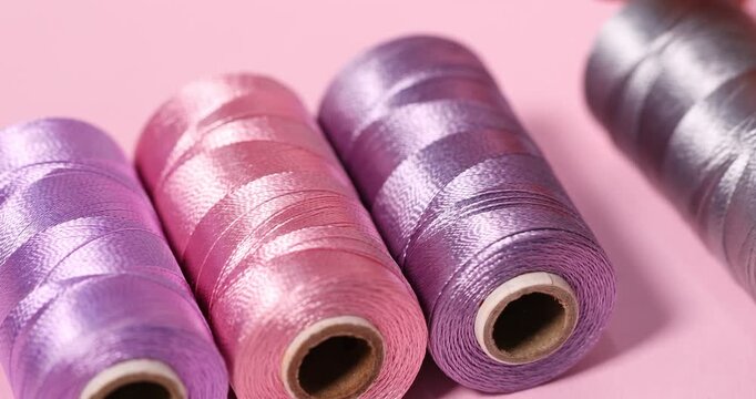 Woman putting spool of thread on pink background, closeup