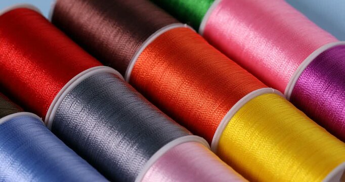 Spools of sewing threads on light blue background, closeup. Camera moving left