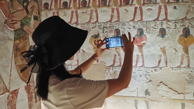 A beautiful tourist wanders inside the tomb of King Seti I, wearing a black hat looking on the inscriptions and drawings carved on the walls of the tomb.